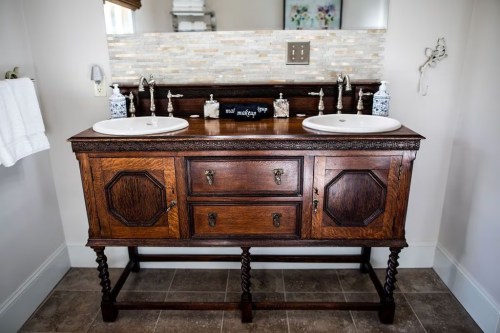 A wooden double sink vanity with two basins, drawers, and a decorative backsplash in a bright bathroom.