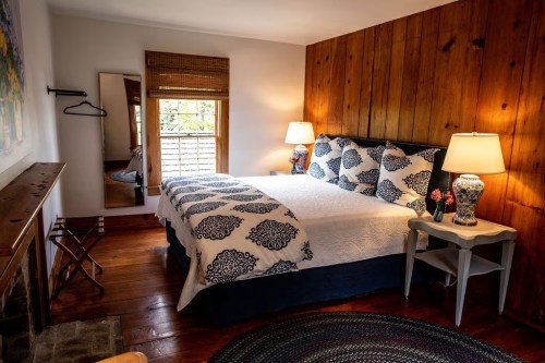 Cozy bedroom with a large bed, wooden walls, lamps, and a mirror, featuring a warm and inviting atmosphere.