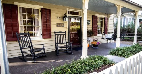A cozy porch with two rocking chairs, potted flowers, and a welcoming entrance to a charming house.