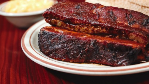 Close-up of two thick slices of smoked barbecue ribs on a plate, with a side of macaroni and cheese in the background.