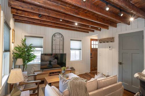 Cozy living room with wooden beams, a TV, plants, and a welcoming entrance. Soft lighting and neutral decor create warmth.