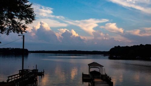 A serene lake at sunset, with clouds reflecting in the water and a small dock in the foreground.