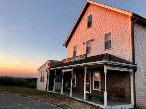 Historic Highland House at sunset, featuring a wooden facade and welcoming porch in Truro, Massachusetts.