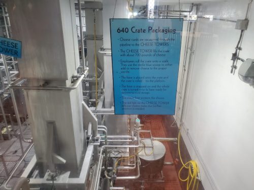 Image of a factory interior with machinery and a blue sign detailing cheese packaging processes.
