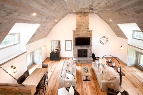 Cozy living room with a stone fireplace, wooden beams, and a dining area, featuring natural light and rustic decor.