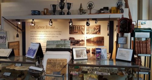 Display of historical artifacts and photographs related to a levee break, with trophies and informational signage.