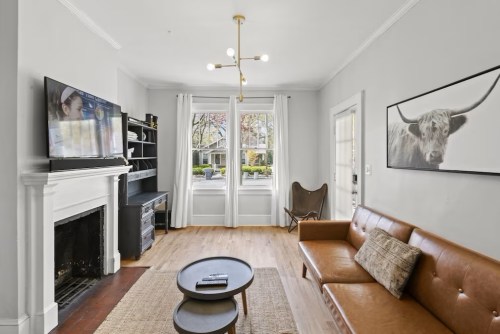 Cozy living room with a leather sofa, modern lighting, a TV, and a large window overlooking a garden.