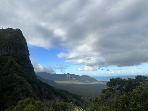 A scenic view of lush mountains under a partly cloudy sky, with valleys and distant hills visible.