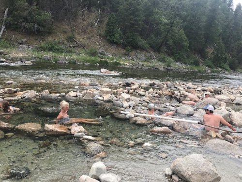 A group of people relaxing in a river, surrounded by rocks and trees, enjoying a sunny day outdoors.