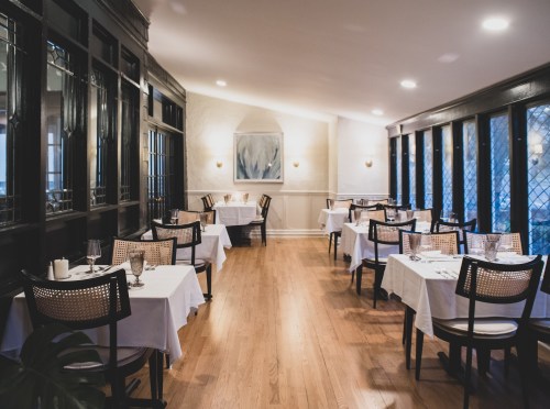 Elegant restaurant interior with white tablecloths, wooden floors, and soft lighting, featuring a cozy, inviting atmosphere.