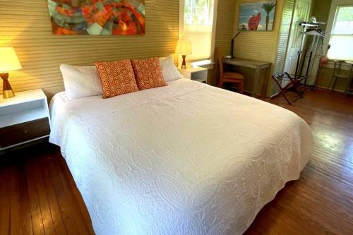 A cozy bedroom featuring a large white bed with orange patterned pillows, wooden floors, and soft lighting.