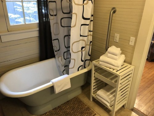 A bathroom featuring a vintage bathtub, a shower curtain, and a white towel rack with neatly stacked towels.