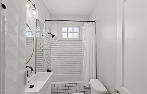 A modern bathroom featuring white subway tiles, a round mirror, and a shower curtain in a bright, minimalist design.