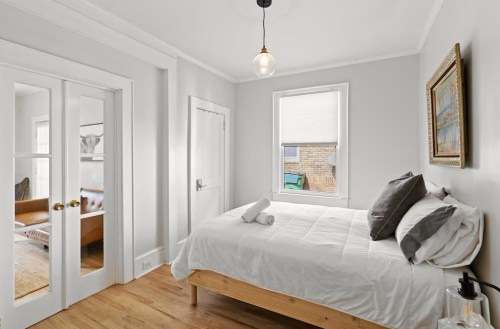 Cozy bedroom with a bed, fresh linens, and a window, featuring light gray walls and wooden flooring.