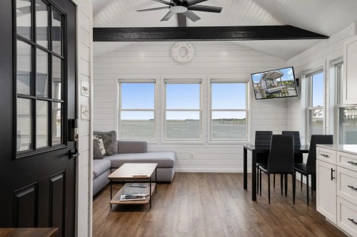 Bright, modern interior of a coastal living space with a sofa, dining area, and large windows overlooking the water.