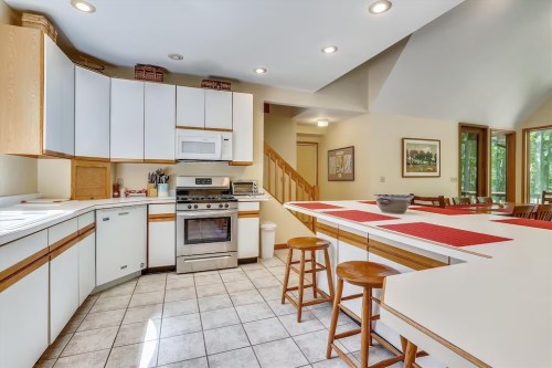 Bright kitchen with white cabinets, stainless steel appliances, and a spacious island with bar stools. Natural light from windows.