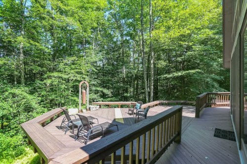 A wooden deck surrounded by lush green trees, featuring chairs and a decorative structure in a serene outdoor setting.