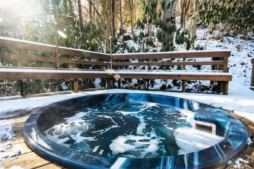 A circular hot tub surrounded by snow-covered trees and wooden decking, creating a cozy winter retreat.