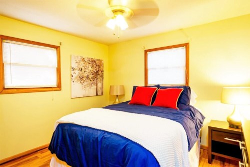 Cozy bedroom with a blue and white bedspread, red pillows, wooden accents, and warm lighting.