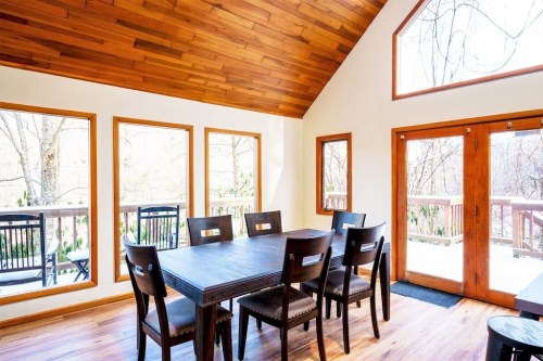 A bright dining area with a wooden table, chairs, and large windows overlooking a snowy landscape.