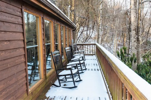 A wooden deck with rocking chairs, surrounded by snow-covered trees and a peaceful winter landscape.