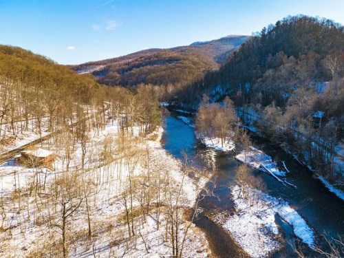 Aerial view of a river winding through a snowy landscape with trees and mountains in the background under a clear blue sky.