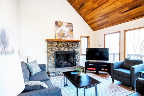 Cozy living room with a stone fireplace, wooden ceiling, TV, and large windows letting in natural light.