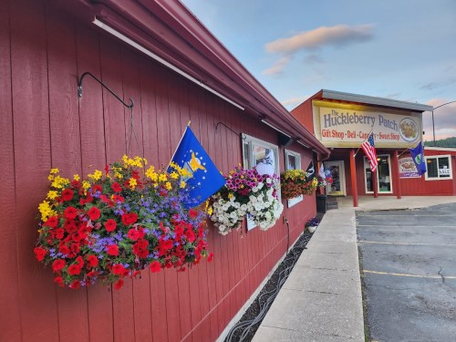 Colorful flower baskets hang from a red building, featuring a sign for the Huckleberry Patch gift shop.