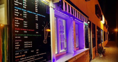 A brightly lit ice cream shop menu with colorful lights and various dessert options displayed outside.