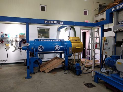 Industrial machinery in a workshop, featuring a blue Pieralisi machine and a yellow component, with tools and a ladder nearby.