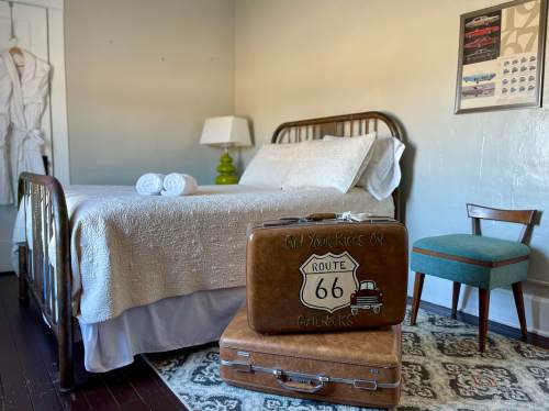 A cozy bedroom with a bed, vintage suitcases, a chair, and a lamp, featuring Route 66 decor.