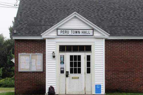 Front view of Peru Town Hall, featuring a brick facade and a white entrance with a sign above the door.