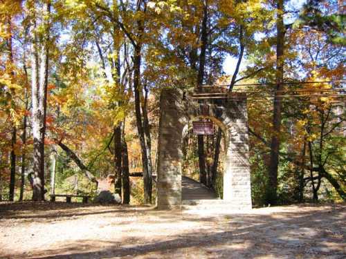 Stone archway surrounded by vibrant autumn trees, leading to a scenic path in a wooded area.