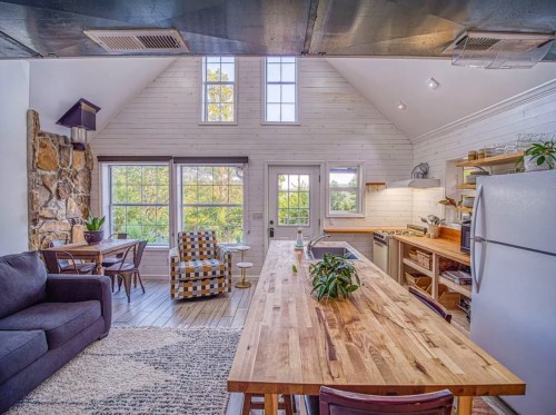 Cozy kitchen and living area with large windows, wooden dining table, and modern decor in a bright, airy space.
