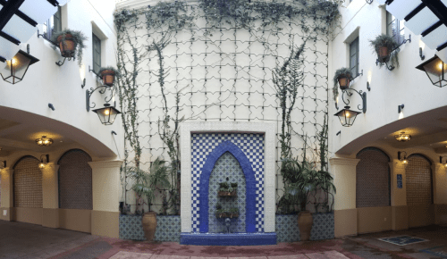 A courtyard with a blue-tiled fountain, surrounded by plants and decorative tiles, under soft lighting.