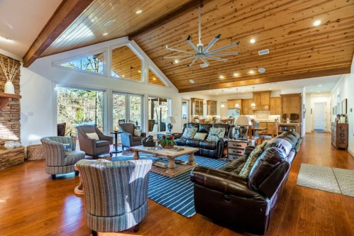 Spacious living room with wooden ceiling, cozy seating, and large windows overlooking nature. Warm and inviting atmosphere.