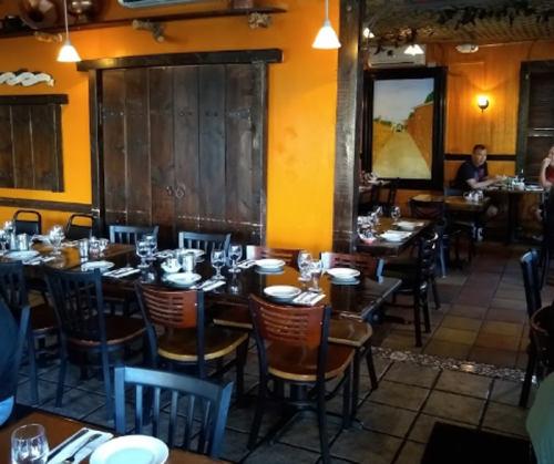 A cozy restaurant interior with wooden tables, chairs, and orange walls, set for dining with plates and glasses.