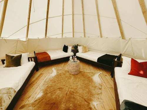 Interior of a cozy tent with circular seating, wooden floors, and decorative pillows, creating a warm atmosphere.
