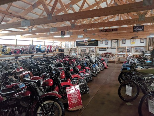 A spacious motorcycle museum filled with various vintage bikes and memorabilia under a wooden ceiling.