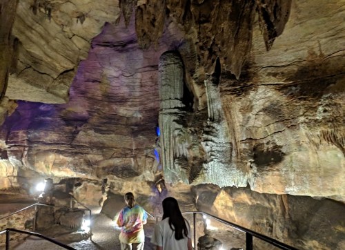 Two people explore a cave with illuminated rock formations and textured walls.