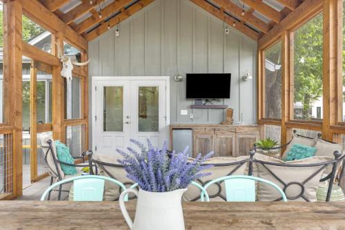 A cozy screened porch with wooden beams, a TV, a small bar, and a table with a vase of lavender flowers.