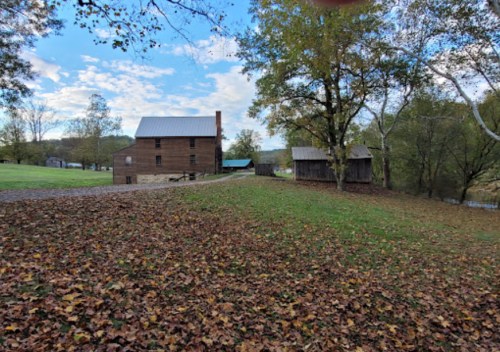 A rustic wooden building surrounded by colorful autumn leaves and trees under a partly cloudy sky.