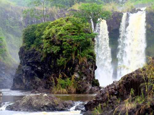 A lush green island surrounded by a waterfall cascading into a river, with mist rising in a tropical landscape.