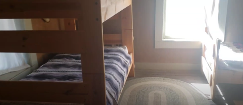A cozy room with a wooden bunk bed, a single bed, and a window letting in natural light.
