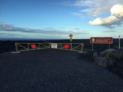 A closed gate at Hawaii Volcanoes National Park, with warning signs and a scenic sky in the background.