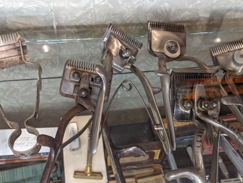 A collection of vintage grooming tools displayed in a glass case, including clippers and scissors.