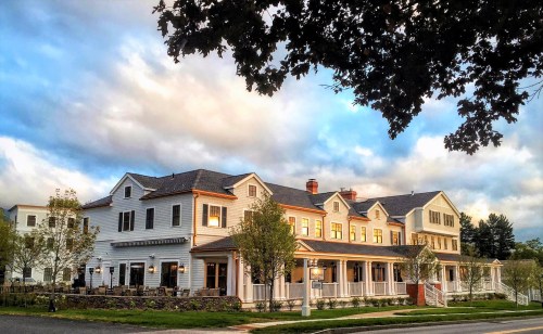 A charming, multi-story white building with a porch, surrounded by trees and a cloudy sky.