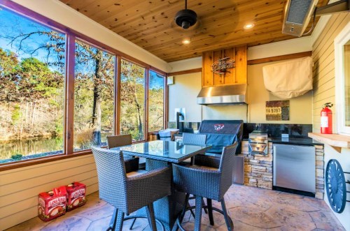 A modern outdoor kitchen with a grill, dining table, and large windows overlooking a scenic view.