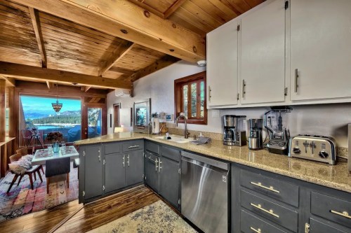 Modern kitchen with dark cabinets, granite countertops, and a view of nature through large windows. Cozy and inviting atmosphere.