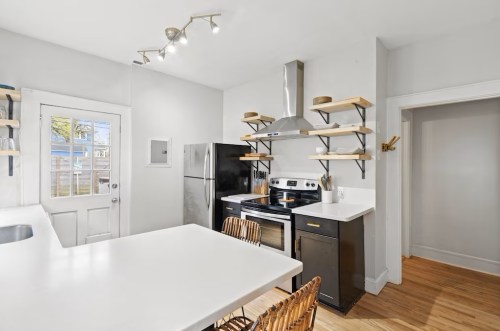 Modern kitchen with stainless steel appliances, open shelving, and a white countertop, featuring a door to the outside.